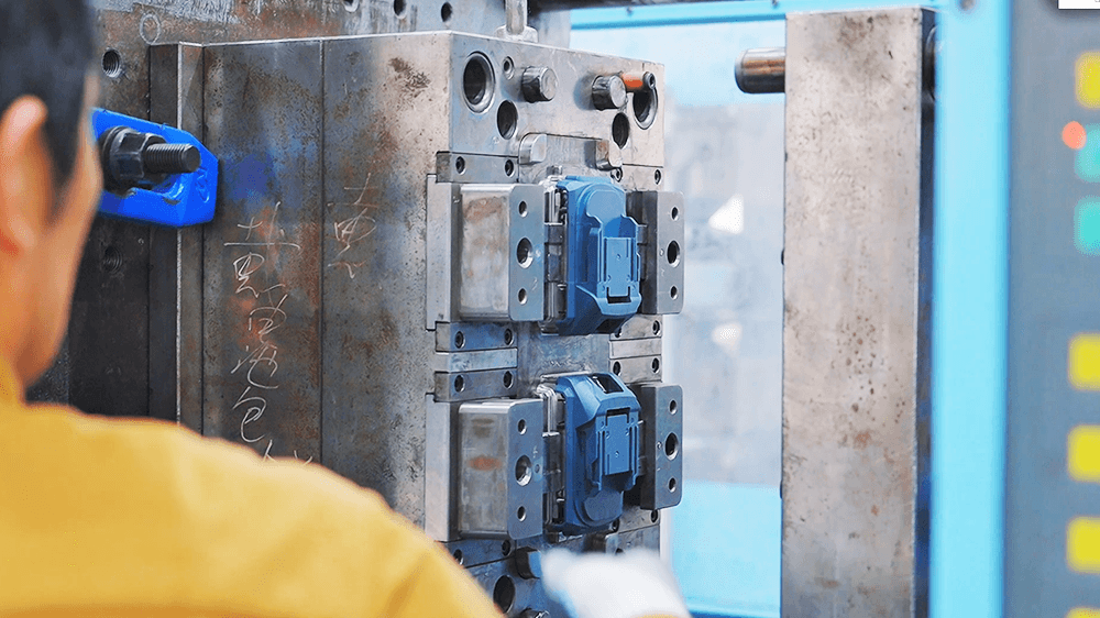 Worker inspecting blue power tool housings in an injection mold