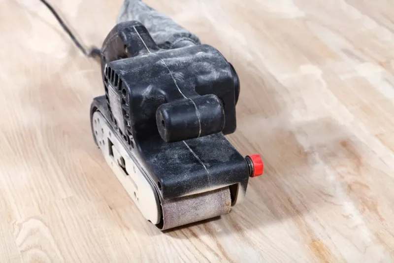 Handheld belt sander on a wooden board