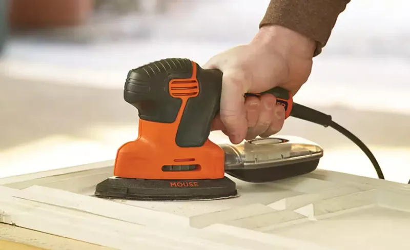 Detail sander positioned on a painted wood panel
