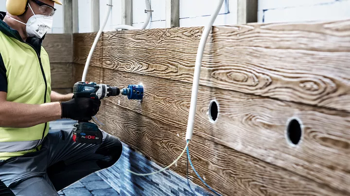 Worker drilling circular openings in a wall with a hole saw