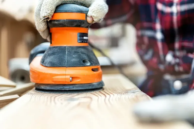 Random orbit sander smoothing a wooden surface